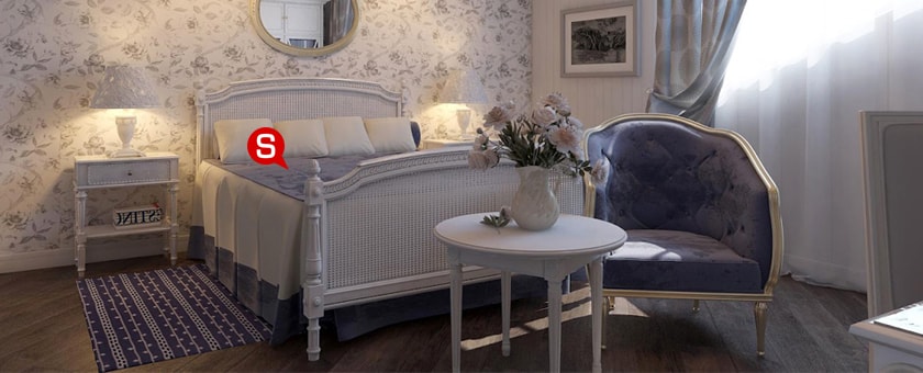 Subtelna sypialnia w stylu prowansalskim z dużym łóżkiem i uroczą, białą szafką nocną. Ścianę ozdabia tapeta w kwiatowy wzór, która nadaje wnętrzu uroku.
